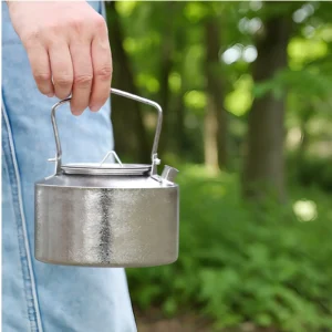 Hand carrying a 1L pure titanium kettle outdoors by the top handle.