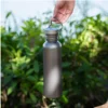 Single-wall titanium water bottle hanging from the metal carry loop outdoors.