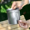 Close-up of a TA1 titanium folding handle mug with lid, volume markings, and side handle detail.