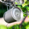 TA1 titanium folding handle mug with lid hanging outdoors, showing the matte titanium finish.