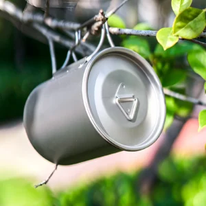 TA1 titanium folding handle mug with lid hanging outdoors, showing the matte titanium finish.