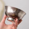 Close-up of TiRoam hammered titanium bowl held by hand, natural titanium finish with textured surface for reusable dining and outdoor meal use.