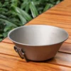 TiRoam pure titanium folding bowl with compact side handle on a wooden outdoor table, lightweight camping cookware for hiking, backpacking, and camp meals.