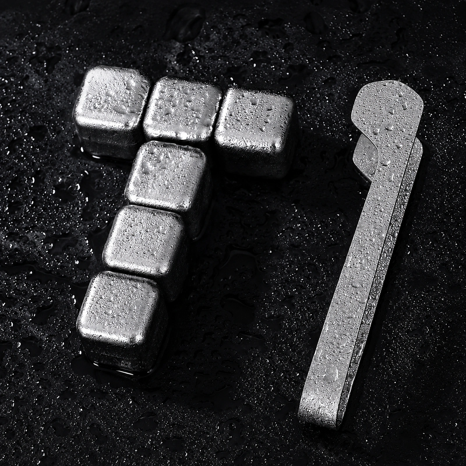 TiRoam six titanium whiskey stones with metal tongs on a wet black surface, reusable ice cubes for whiskey, cocktails, and chilled drinks.