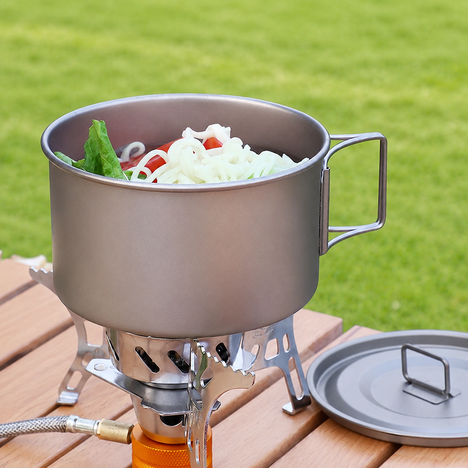 TiRoam titanium camping pot cooking noodles on a camp stove with lid beside it, lightweight titanium cookware for outdoor meals and backpacking.