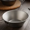 Close-up of TiRoam pure titanium folding bowl with side handle on a tabletop, durable lightweight outdoor bowl for camping, cooking, and backpacking gear.