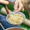 TiRoam titanium folding bowl filled with noodles and held by its foldable handle, lightweight camping bowl for outdoor cooking, backpacking, and trail meals.
