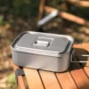 TiRoam titanium lunch box with lid closed on a wooden camping table, compact outdoor cookware and food container with folding handle for easy packing.