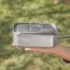 iRoam titanium lunch box with lid held by hand outdoors, compact lightweight titanium container for camping, travel, meal prep, and outdoor dining.