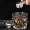 TiRoam titanium whiskey stone held with tongs above a whiskey glass, reusable metal ice cube for cooling drinks without dilution.