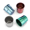 Top-down flat lay view of a four-color TiRoam anodized titanium cups set scattered on a clean white background.