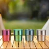 Four colorful TiRoam anodized titanium stackable cups in purple, green, blue, and silver lined up on a wooden camping table.