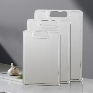 Three sizes of grooved pure titanium cutting boards displayed upright on a kitchen counter.