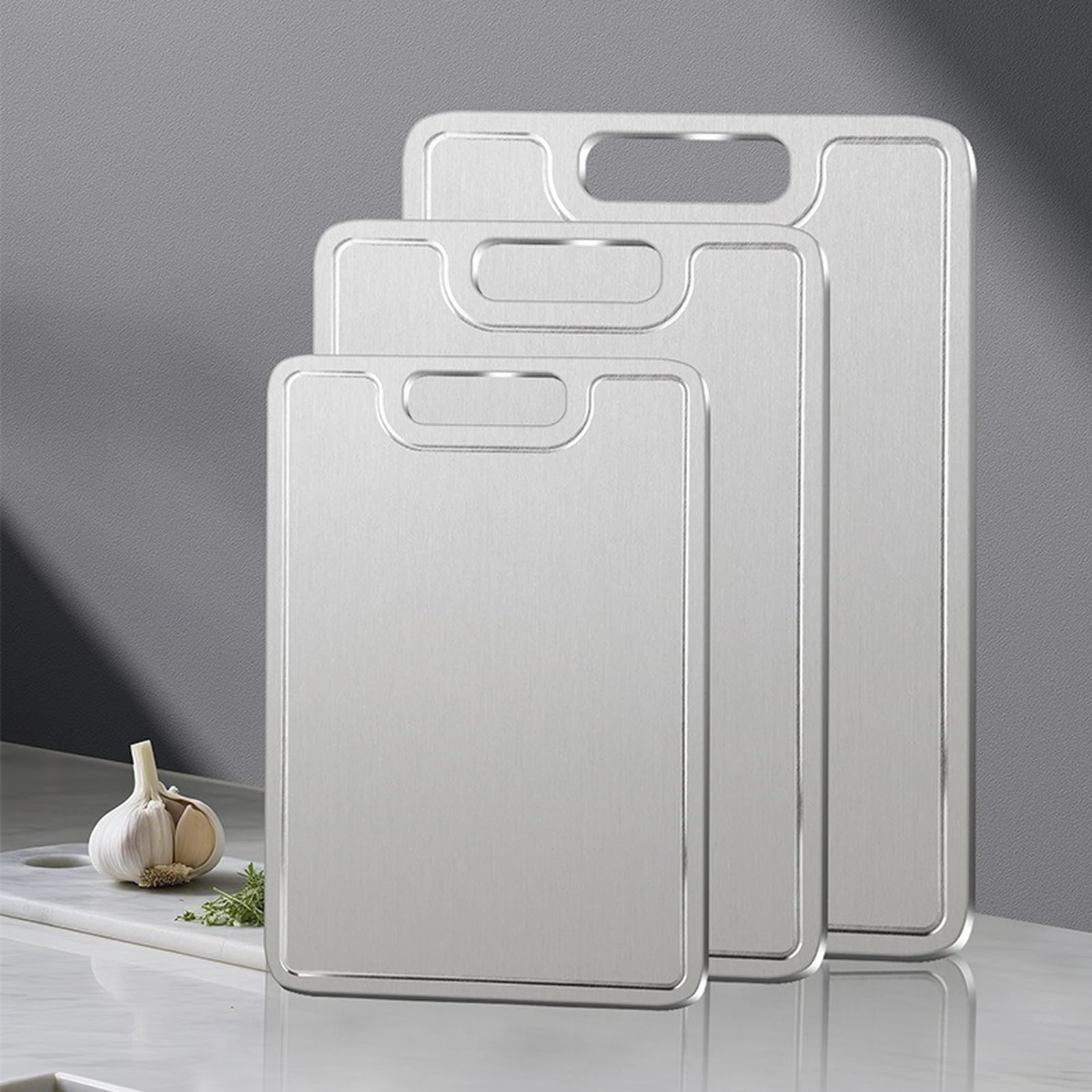 Three sizes of grooved pure titanium cutting boards displayed upright on a kitchen counter.