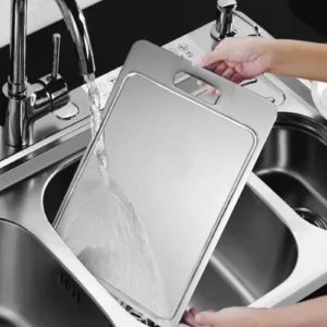 Grooved pure titanium cutting board being rinsed under running water in a kitchen sink.