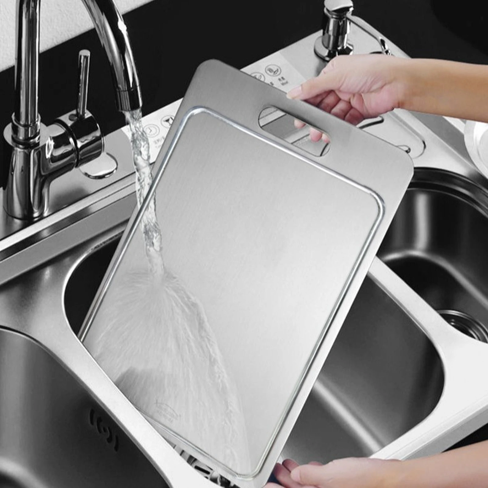 Grooved pure titanium cutting board being rinsed under running water in a kitchen sink.