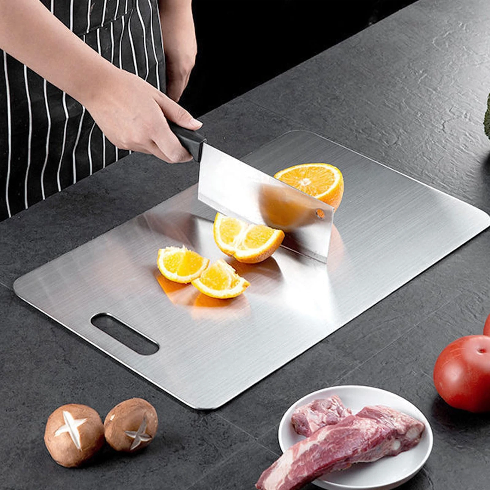 Pure titanium cutting board used for slicing fresh oranges during kitchen food prep.
