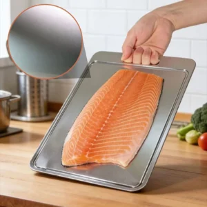 Grooved pure titanium cutting board holding a large salmon fillet in a kitchen.