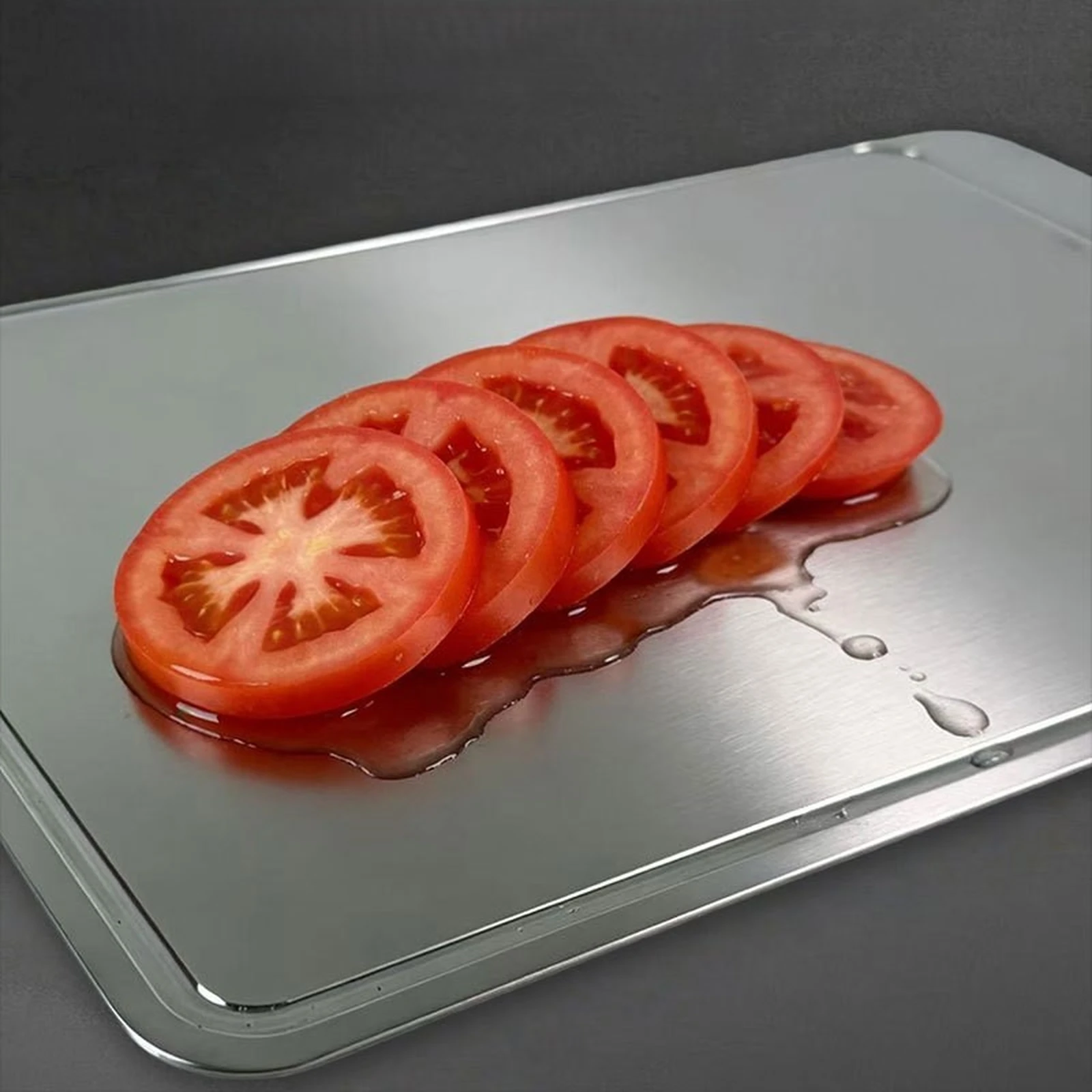 Sliced tomatoes on a pure titanium cutting board with a raised groove around the cutting surface.