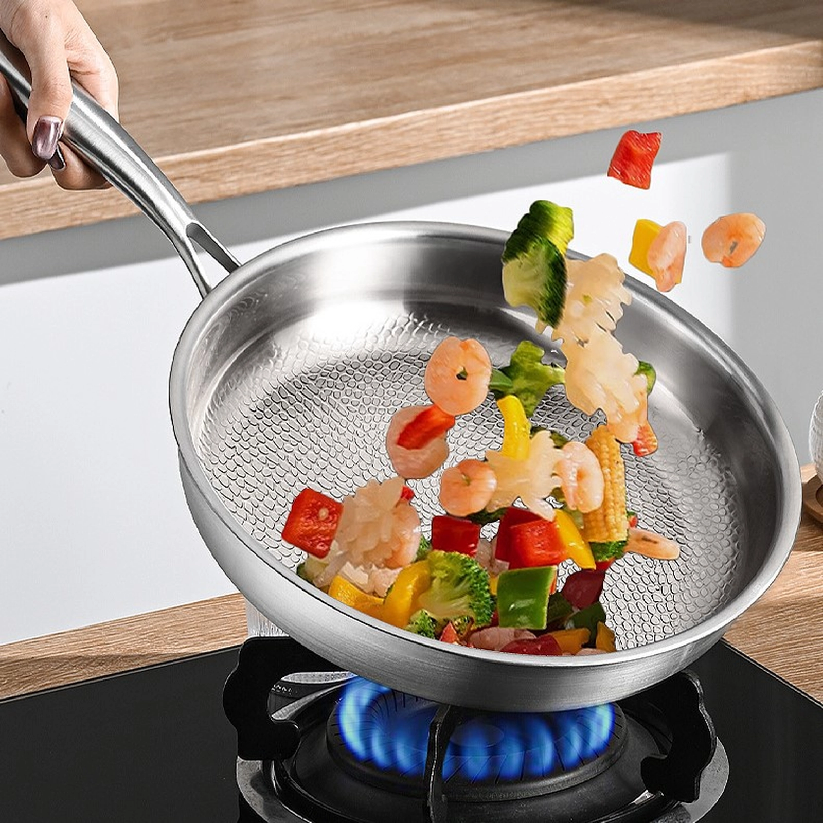 Shrimp and vegetables being tossed in a titanium frying pan over a gas flame