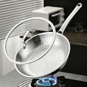 Dragon-scale titanium frying pan with a stainless steel and glass lid displayed above a gas burner.
