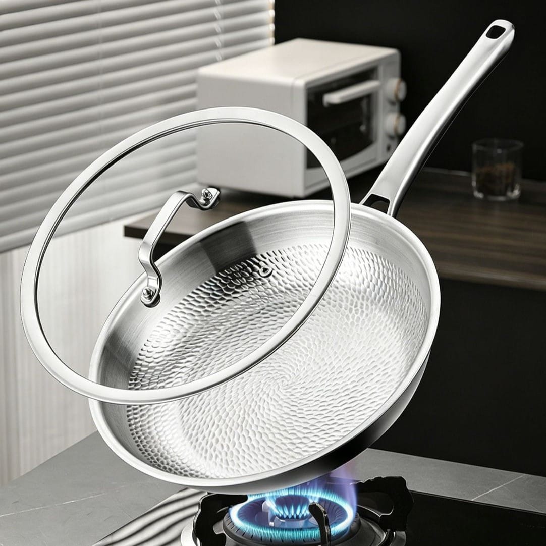 Dragon-scale titanium frying pan with a stainless steel and glass lid displayed above a gas burner.