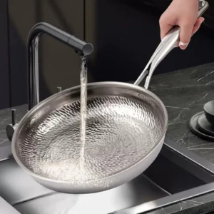 Water rinsing the textured cooking surface of a titanium frying pan under a kitchen faucet.