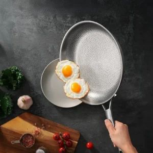 Two fried eggs sliding from a textured titanium frying pan onto a plate during meal preparation.
