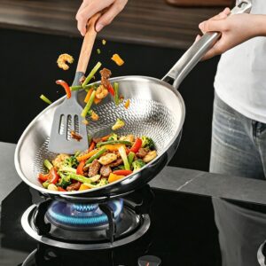 Shrimp, vegetables, and meat being tossed in a textured titanium frying pan on a gas stove.