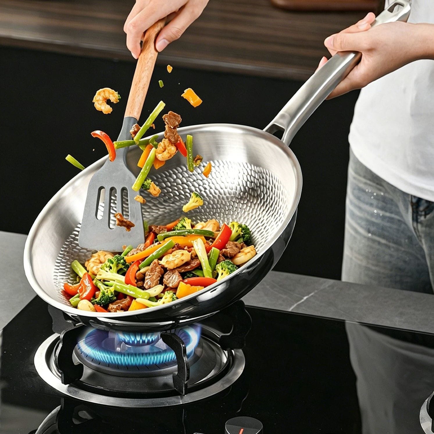 Shrimp, vegetables, and meat being tossed in a textured titanium frying pan on a gas stove.